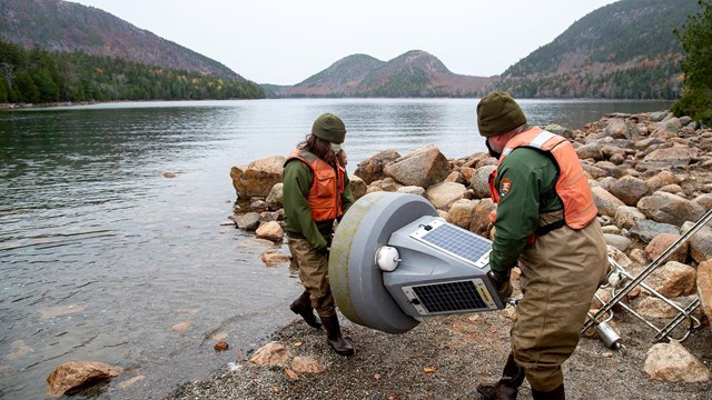 two staff members walk toward lake holding a buoy