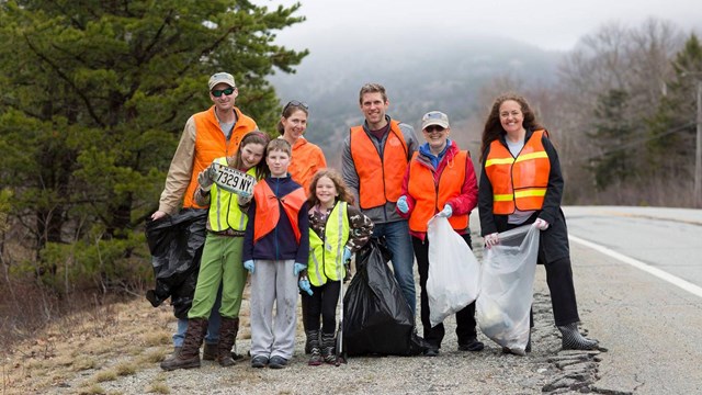 a group stands on a road side in the rain cleaning up trash