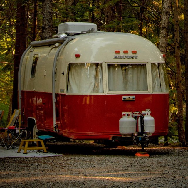 Photo of a white and red vintage trailer under trees at a campsite. 