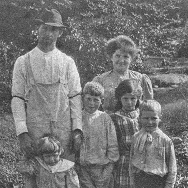 A black and white image of two adults posing with four children, all in old fashioned clothes