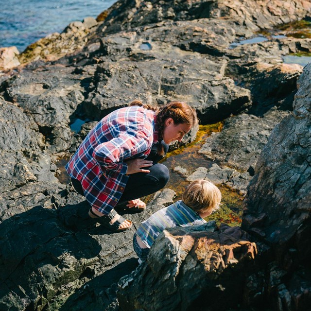 Woman and child explore pools and crevices in rocks along coastline