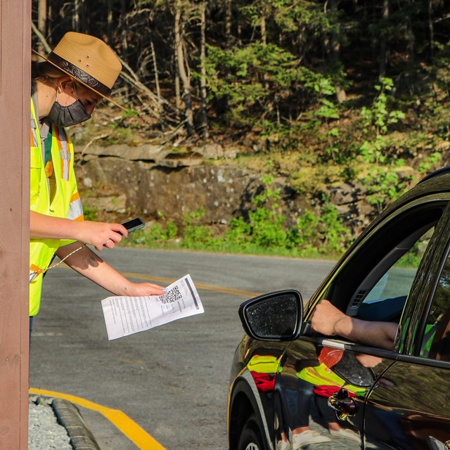 Ranger leans out of booth window to scan a device held by a driver of a vehicle.