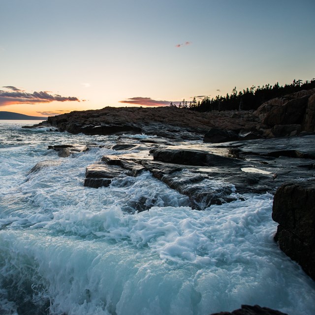 Waves crash against rocky coastline at sunset