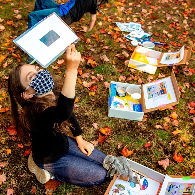 A child sits on a lawn near science kits while looking at a sample sheet
