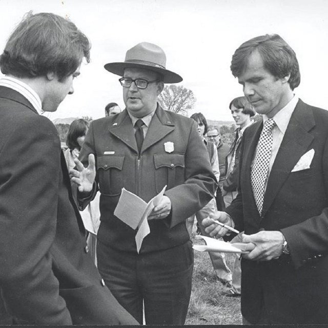 Black and white photo of 3 men in business suits discussing. 