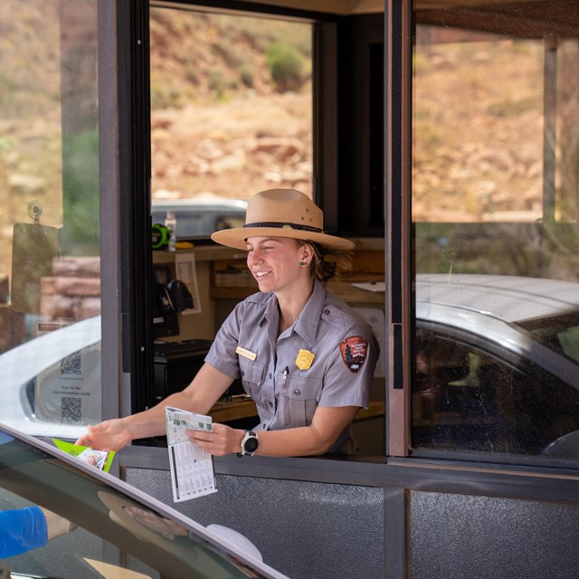 Photo of a female park ranger in uniform working in an entrance booth.