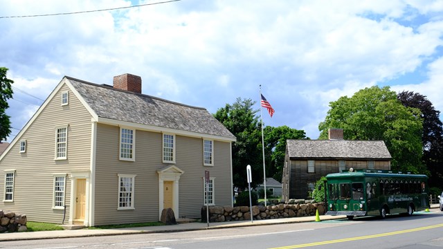 A trolley sits in front of two historic 2-story wooden homes