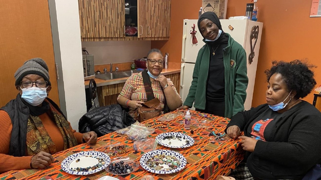 Four women surround a table of beads.