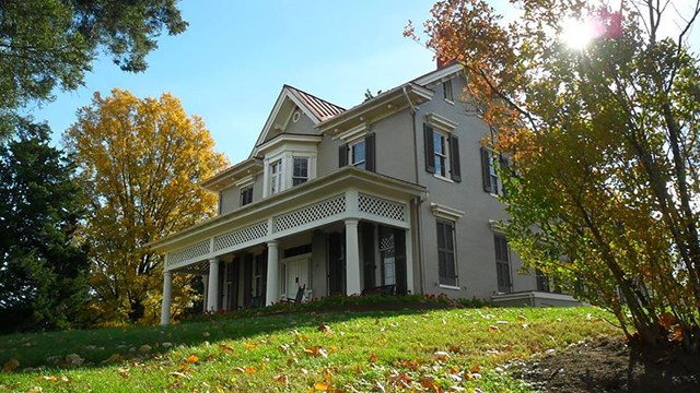 two story house with porch on a grassy hill
