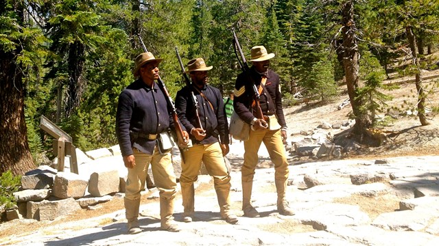 3 Buffalo Soldiers impersonators pose in front of trees