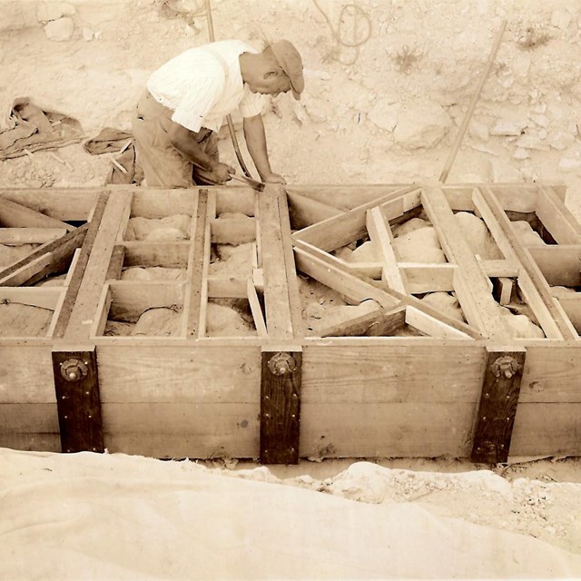 Man kneels to work on large rectangular crate around rock