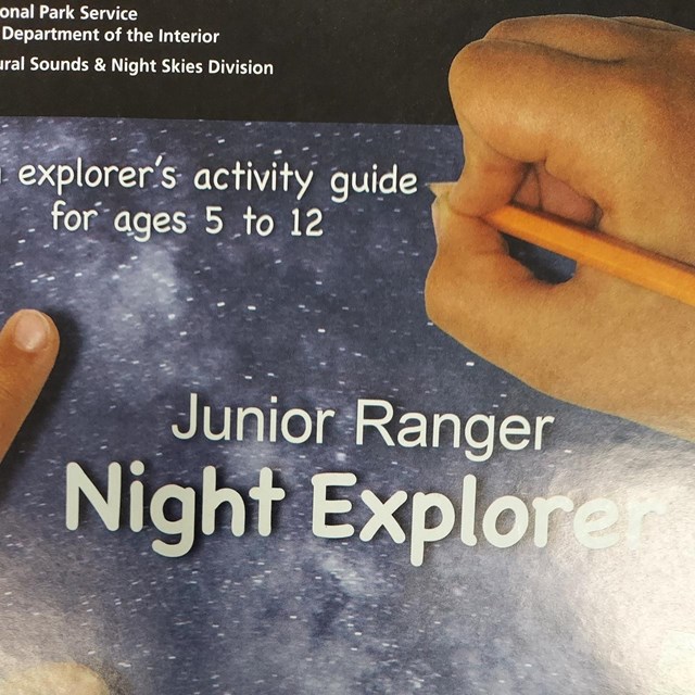 The Milky Way over silhouetted hills fills the background of the NPS Night Explorer book.