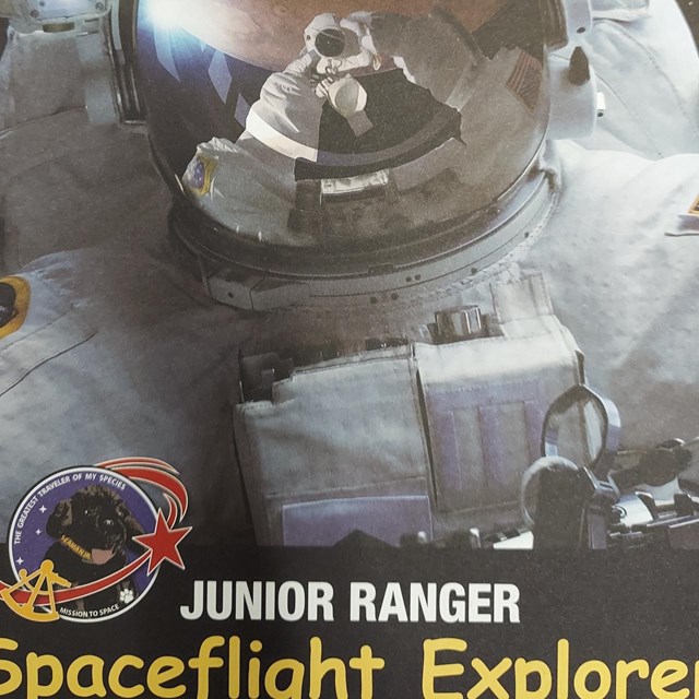 An astronaut in a full space suit takes a selfie in front of a planet on the cover of the NPS book.