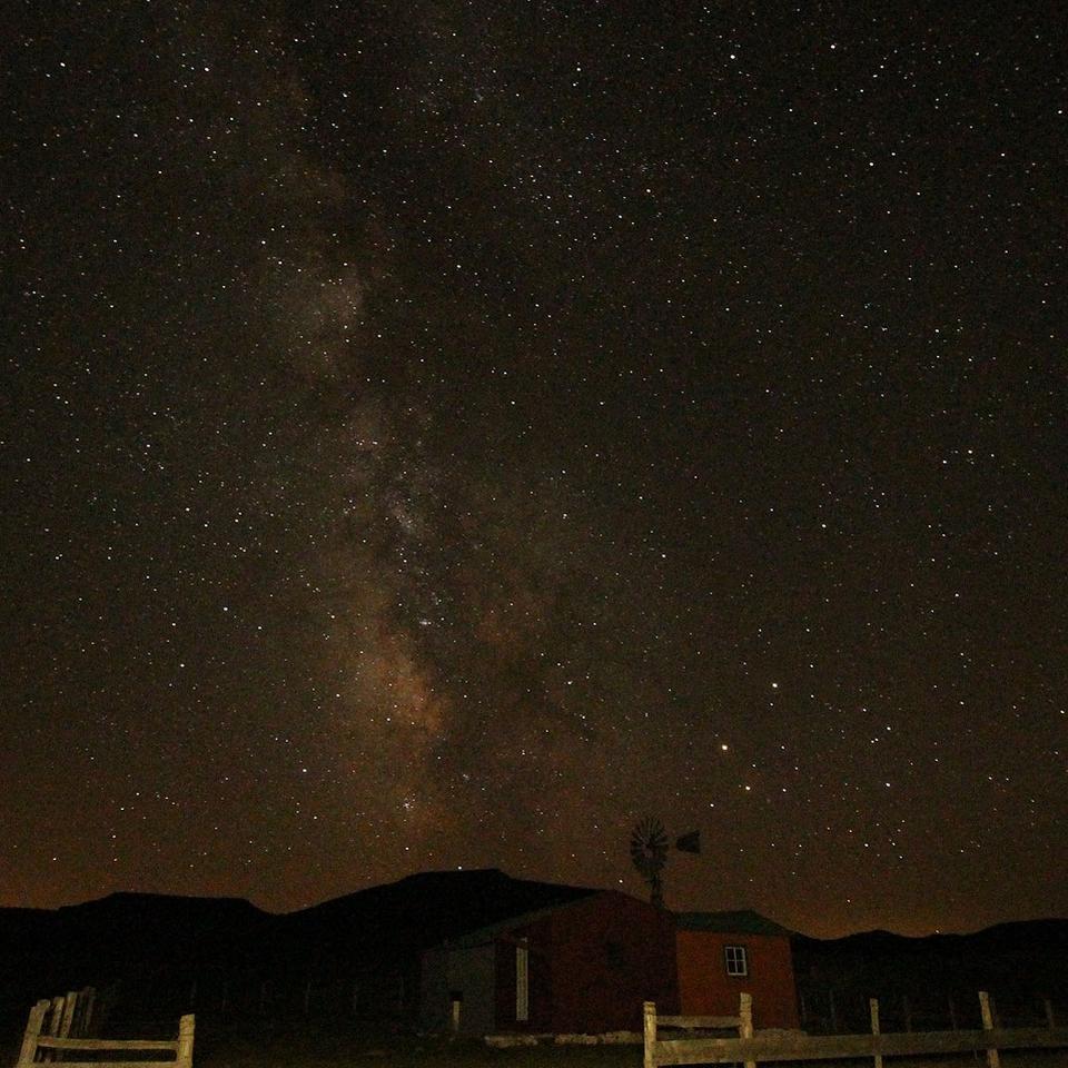 Mixture of dotted lights & streaks form a vertical line around a black sky over a cabin.