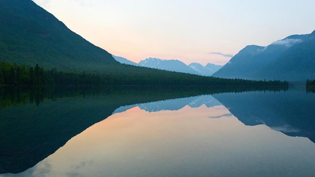 A large lake's glassy surface reflects the mountains and sky.