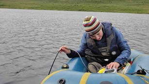 A woman in an inflatable raft takes measurements of water quality.