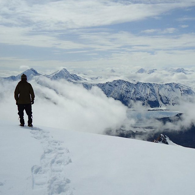A hiker in winter snow high over a glacier and fjord.