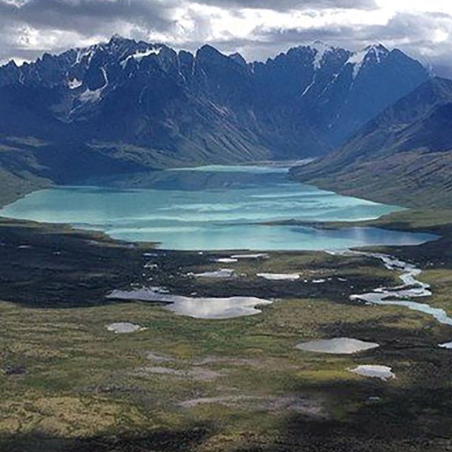 An aerial view of a turquoise lake, river, and mountains.