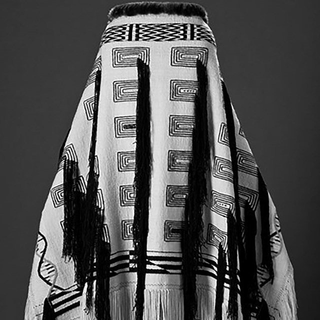 Image of a Alaskan Native Robe. It has fringes on  bottom with vertical stands hanging down.