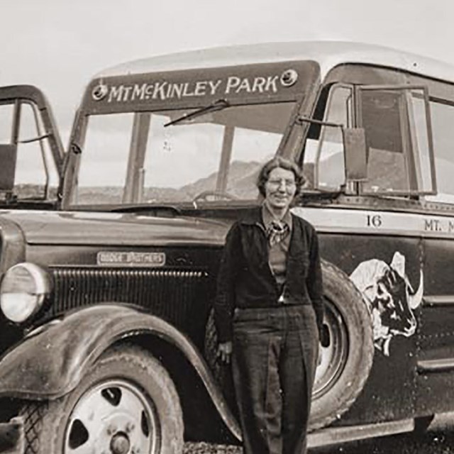 A woman poses in front of a bus.