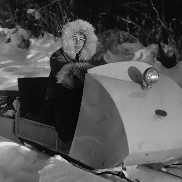 A woman drives a snow machine pulling a sled.