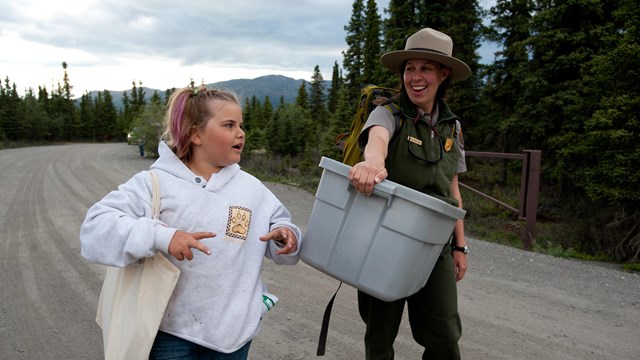a park ranger in Denali speaks with a young girl while carrying supplies
