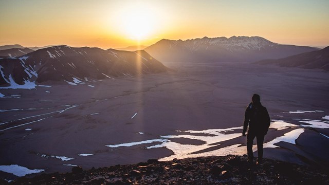 a hiker stands on a ridge watching sunset over a river valley