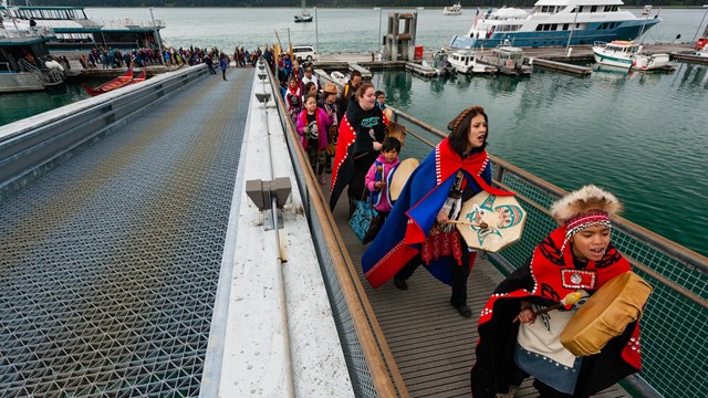 a group of indigenous members play instruments to celebrate a totem pole raising in Glacier Bay NP