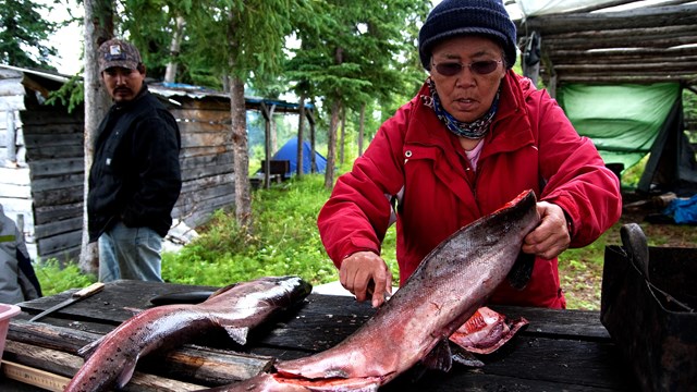 A women cleans fish on wooden planks with a man watching in the background