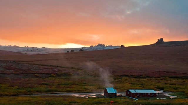 two small buildings with steam emerging from them in the tundra at sunset in Bering Land Bridge