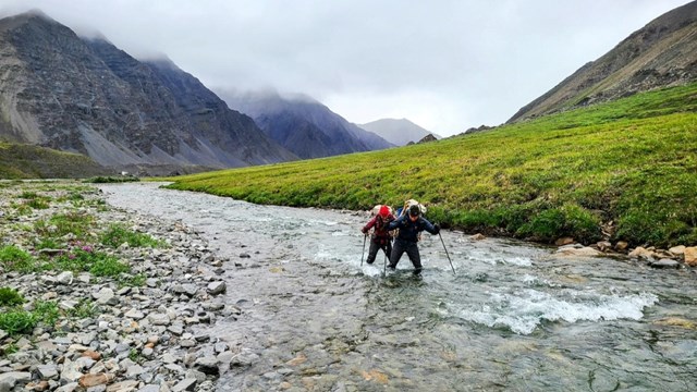 Two backpackers cross a creek in the mountains