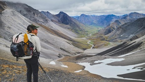 A park ranger with backpack standing on a high ridge overlooking a mountain valley