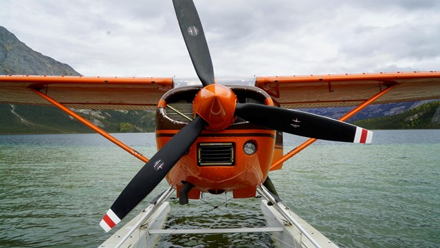 front view of orange floatplane with black propellers on a mountain lake