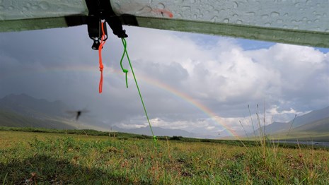 view looking under a tent fly at a rainbow and rainstorm in a mountain valley