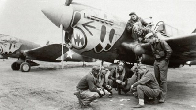 black and white image of a crew in flight gear playing a game underneath a plane