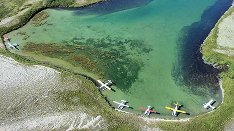 float planes docked along the shore of an inlet in turquoise waters