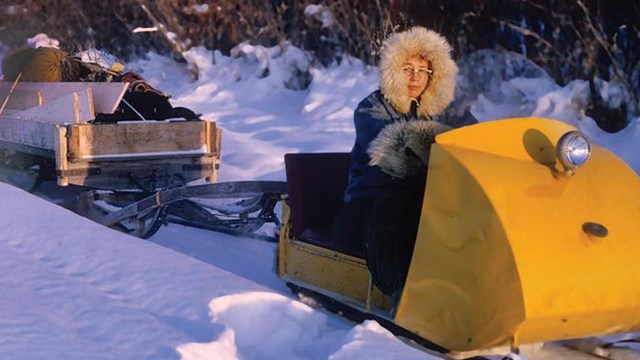 woman driving an old snowmobile, pulling a sled