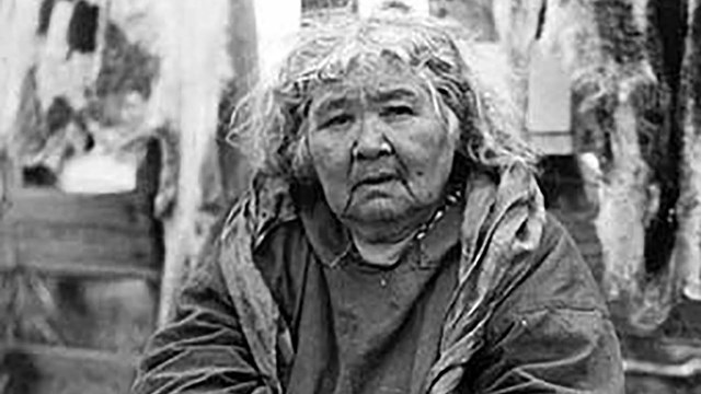 A woman sits gazing at camera. She has long white hair.
