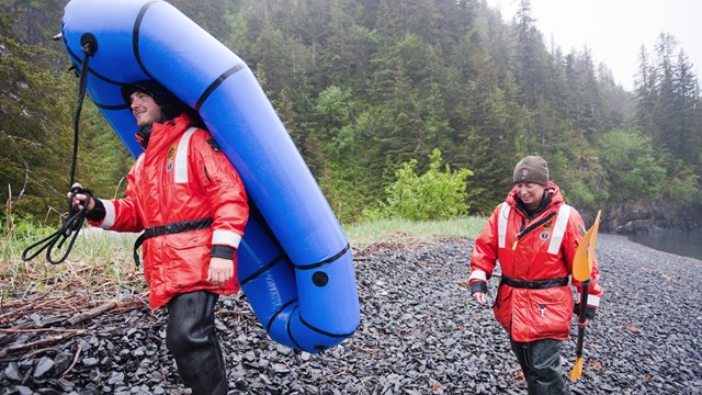 two NPS employees carry an inflatable raft along a beach in the rain