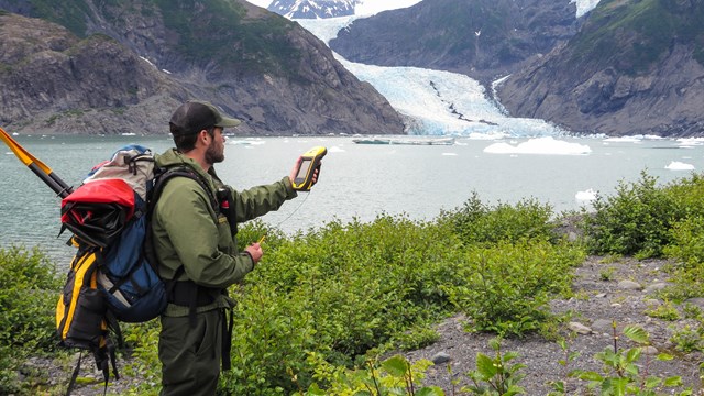 a NPS staff member takes GPS coordinates in front of a glacial lagoon