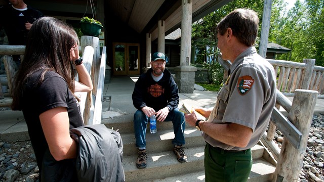 two park visitors speak to a park employee while sitting outside the visitors center of Denali NP
