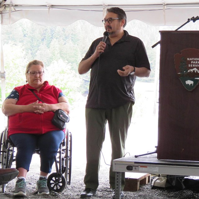  A woman in a wheelchair and a man on a stage.  They are next to a podium.