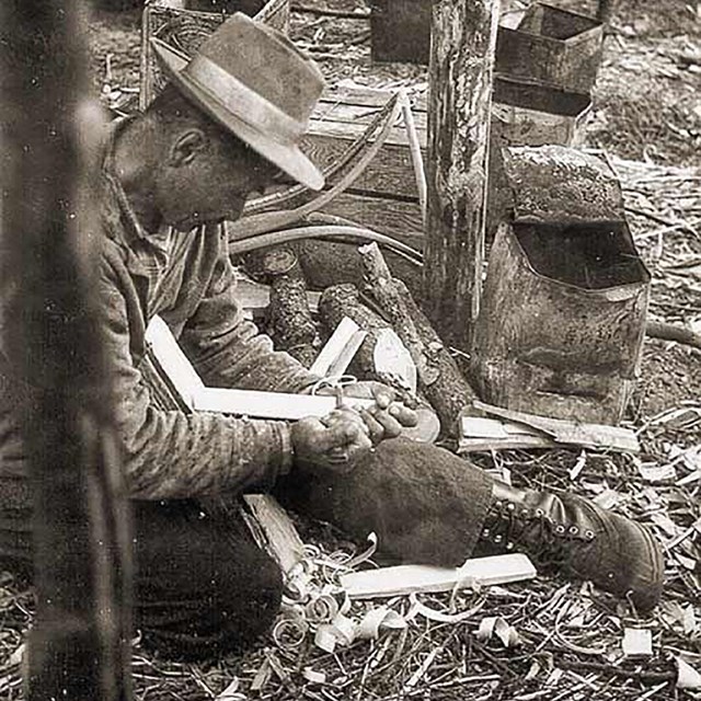 A man sits on the ground sharping tools