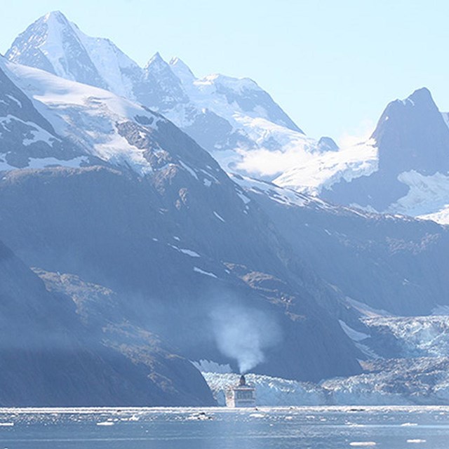 a cruise ship travels near a glacier and mountain peaks