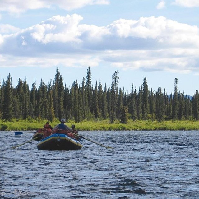 a raft floats down a wide river surrounded by trees