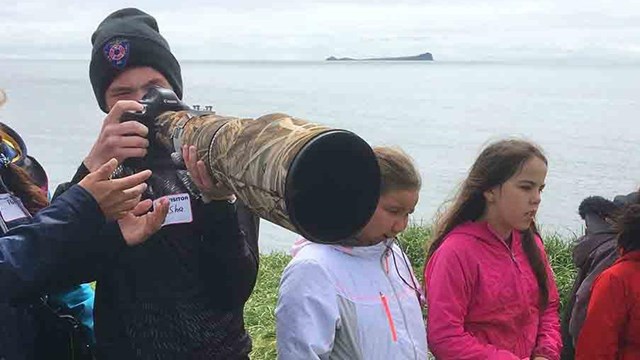 Youth stand on a coastal cliff photographing birds.