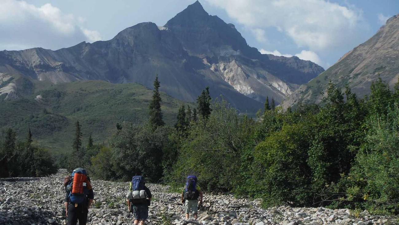 Backpackers hike up a rocky stream bed to the mountains.