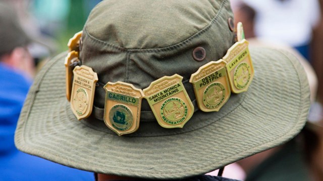 Person in bucket hat, brim lined with golden junior ranger badges.