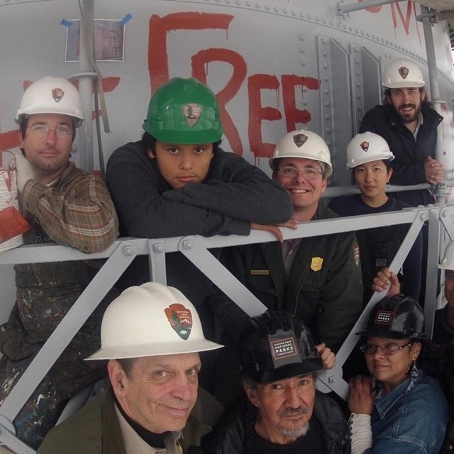 Group of indigenous people and National Park Service employees pose on water tower scaffolding.