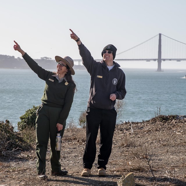 A ranger and a volunteer on Alcatraz pointing, with the Golden Gate Bridge in the background